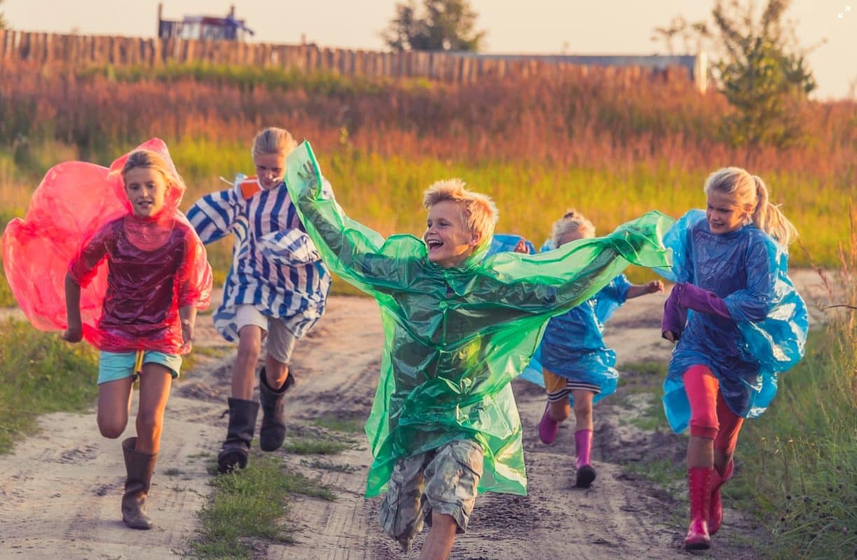 χαρούμενα παιδιά που τρέχουν με πολύχρωμο αδιάβροχο